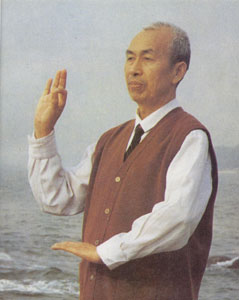 Tian Ruisheng in a white shirt and red vest, one hand raised, by the sea